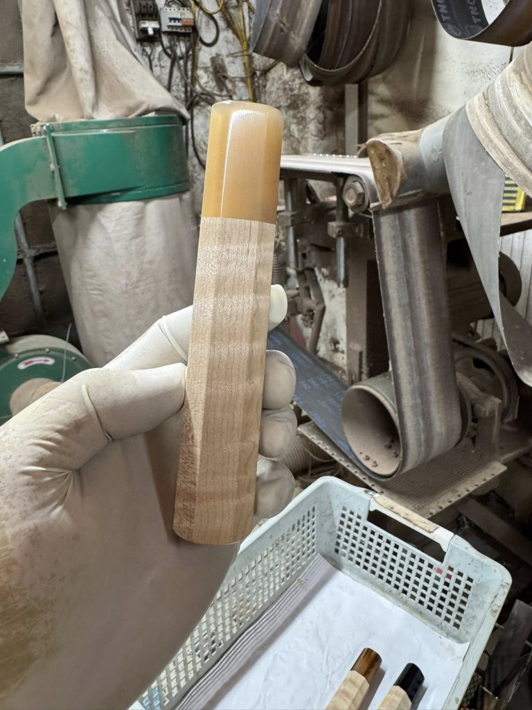 Pale figured wooden handle with a light amber front ferrule, held in a white glove near workshop equipment.