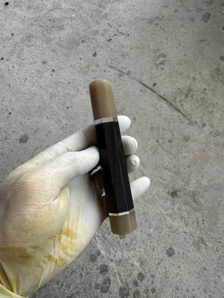 African blackwood handle with a pale horn front ferrule, separate pale horn rear end cap, and thin silvery spacers, held in a white glove.