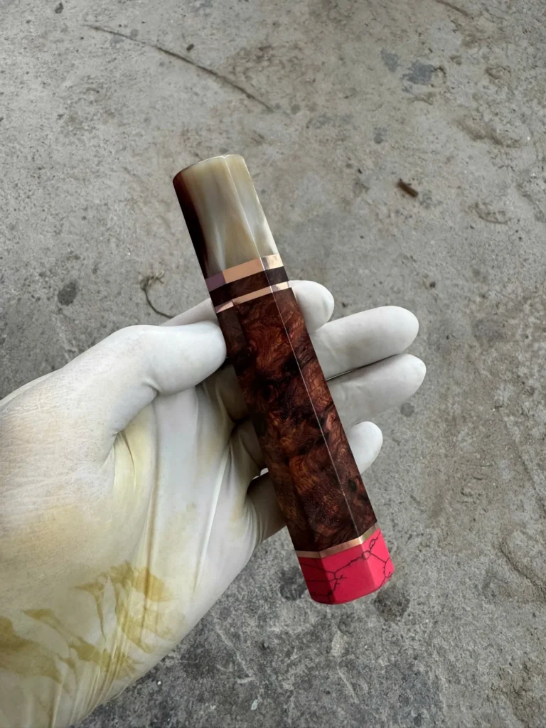 Reddish figured Amboyna burl handle with a pale marbled horn front ferrule, metallic spacers, and pink coral rear end cap.