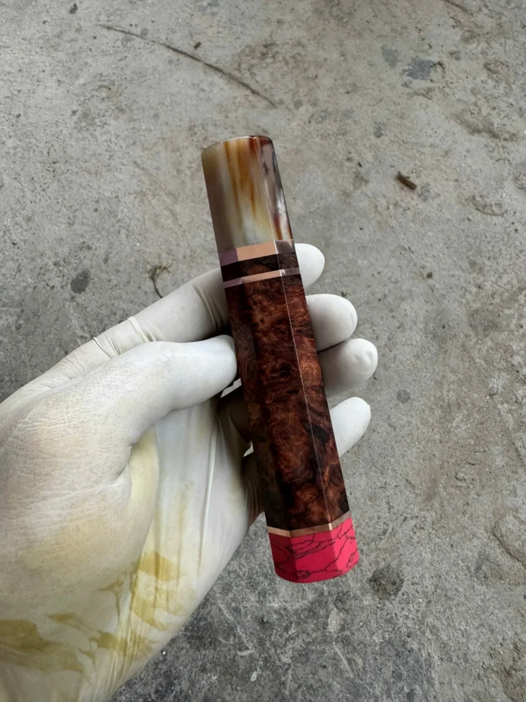 Amboyna burl handle with a cream-and-amber marbled horn front ferrule, bright metallic spacers, and a pink coral rear end cap.