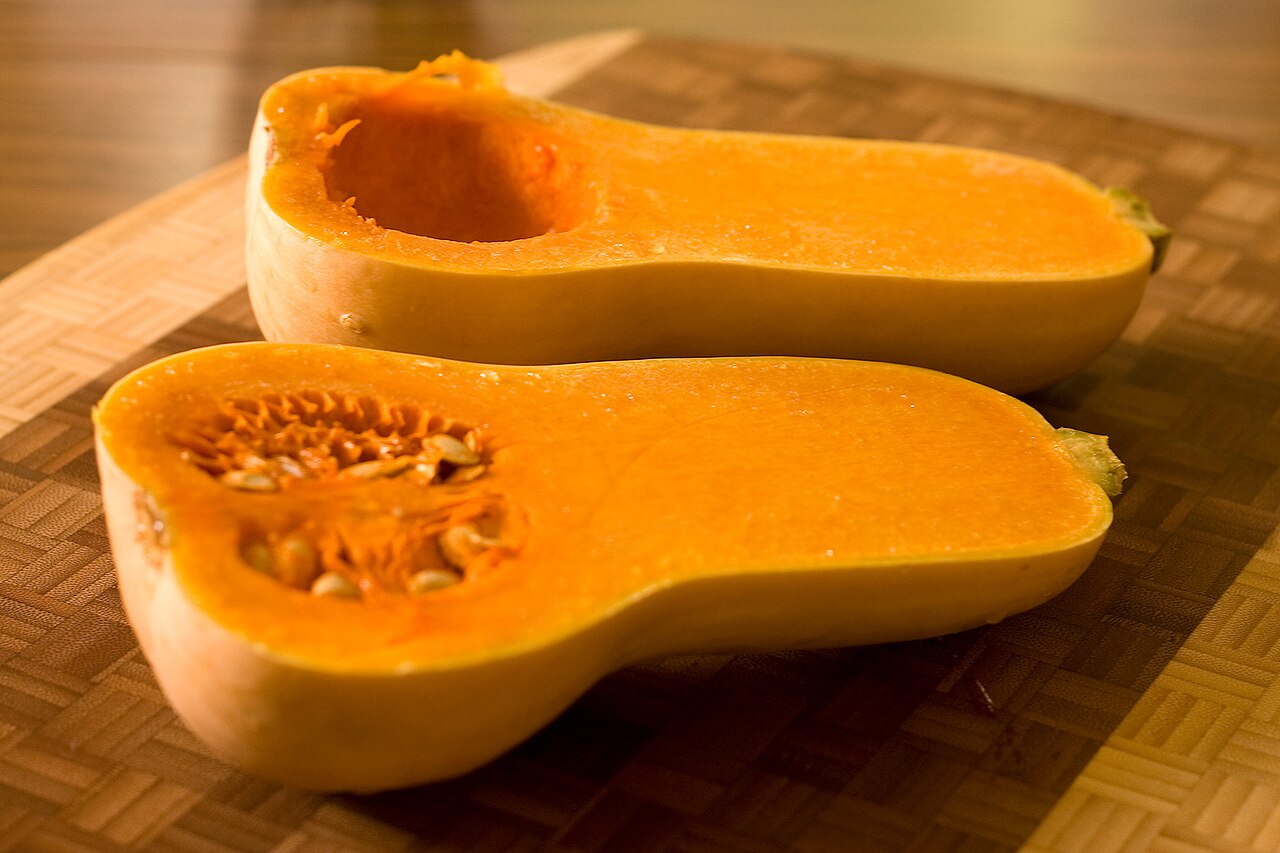 Two lengthwise halves of a butternut squash show the seed cavity in the bulb end.