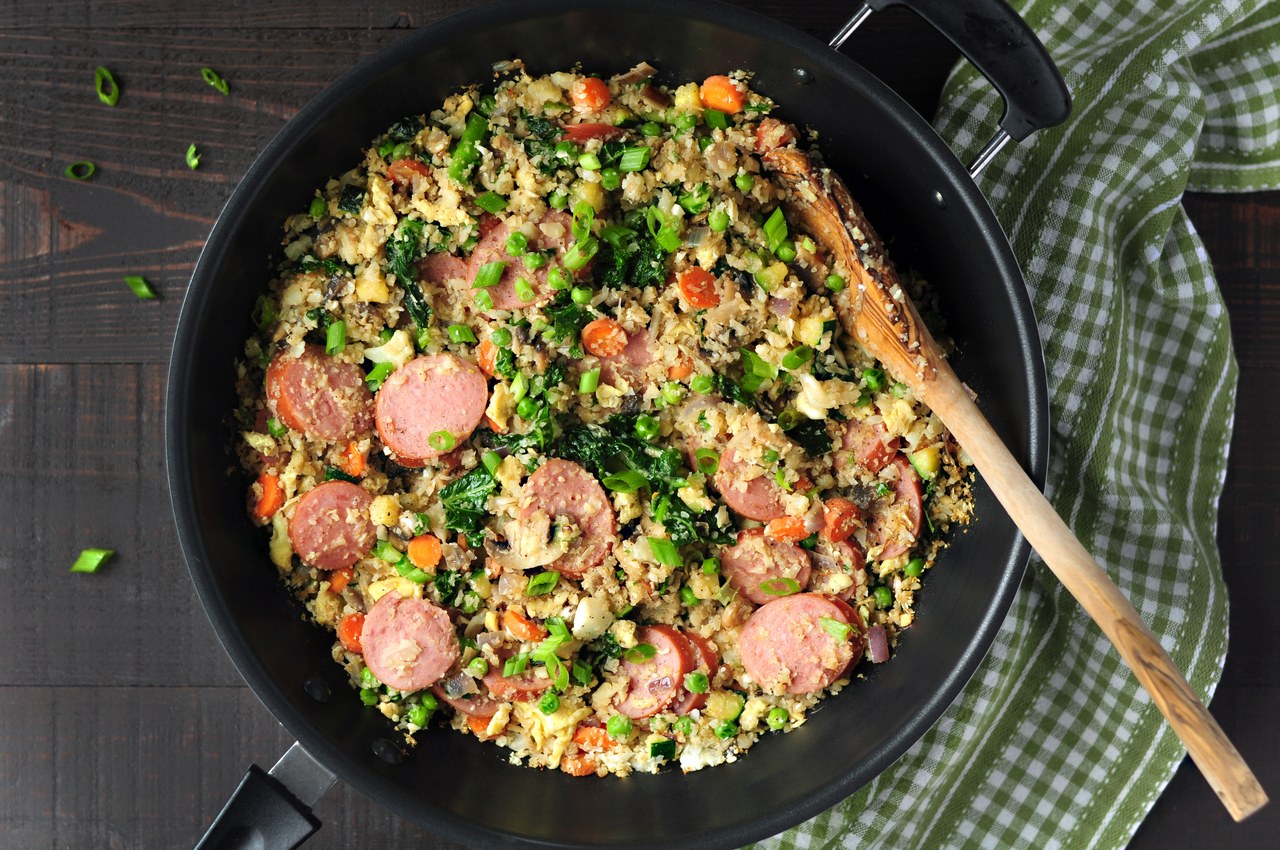 Cooked cauliflower fried rice with sliced sausage and vegetables in a skillet