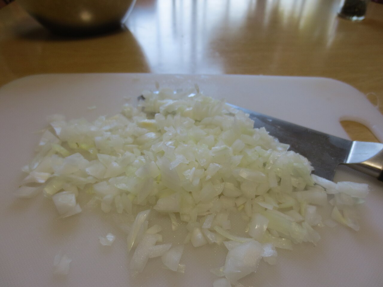 Diced onion pieces on a cutting board beside a kitchen knife.