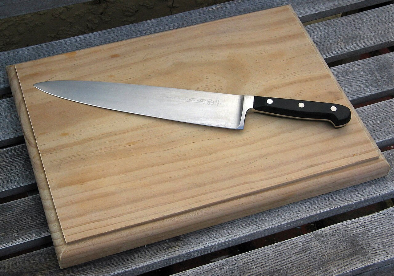 A chef’s knife laid diagonally across a rectangular wooden cutting board.