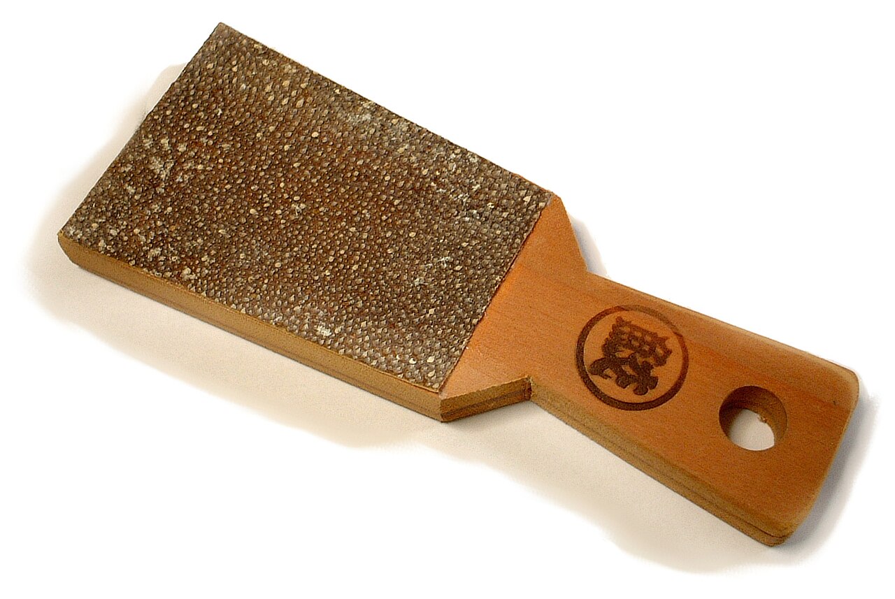 A rectangular sharkskin-style wasabi grater mounted on a wooden paddle.