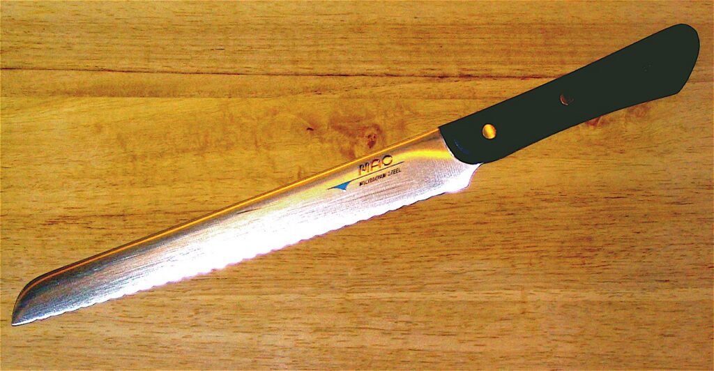 MAC bread knife with a long serrated blade on a wooden board