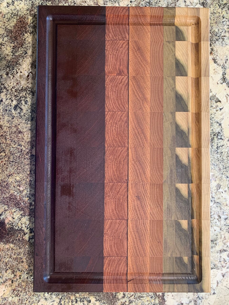 A rectangular end-grain cutting board with contrasting wood blocks and a perimeter groove.