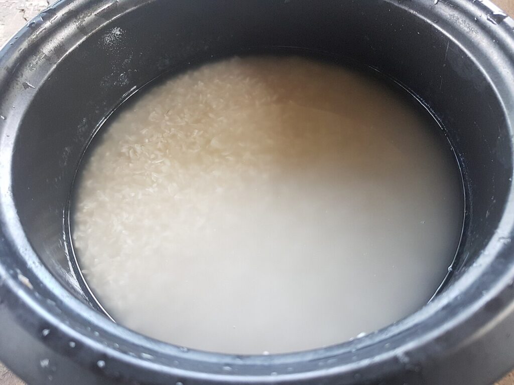 Uncooked rice submerged in cloudy rinse water