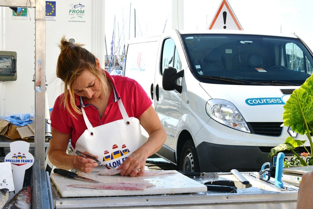 A demonstrator holds fish-bone tweezers above a fillet supported on a cutting board