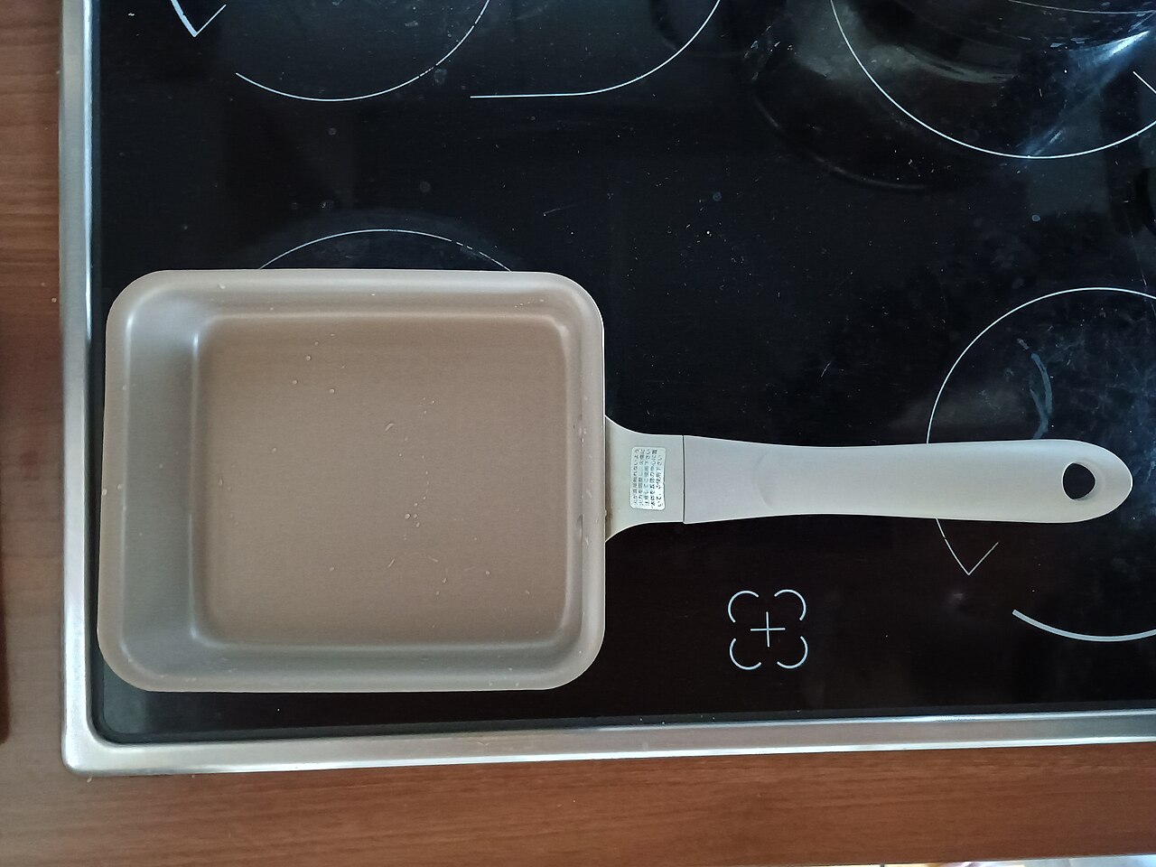 Square egg pan with straight sides and a long handle on a hob