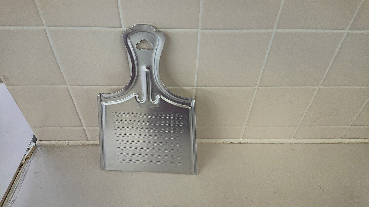 A flat metal Japanese grater with rows of small raised teeth and an integral handle.