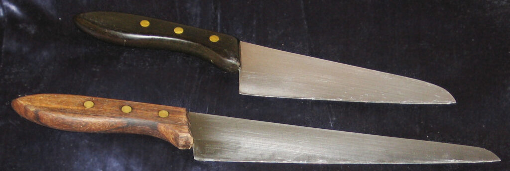 Two used santoku knives showing scratched blades and wear around the handles