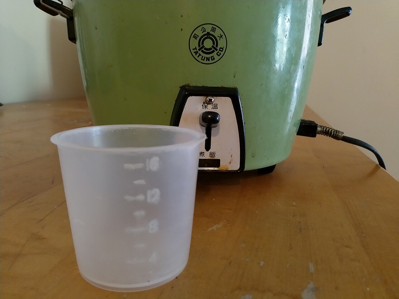 Translucent rice measuring cup in front of a rice cooker