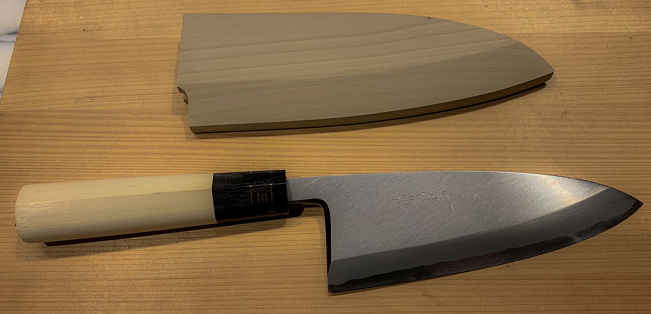 Ginsan deba knife beside a wooden saya at Jikko Knives in Sakai