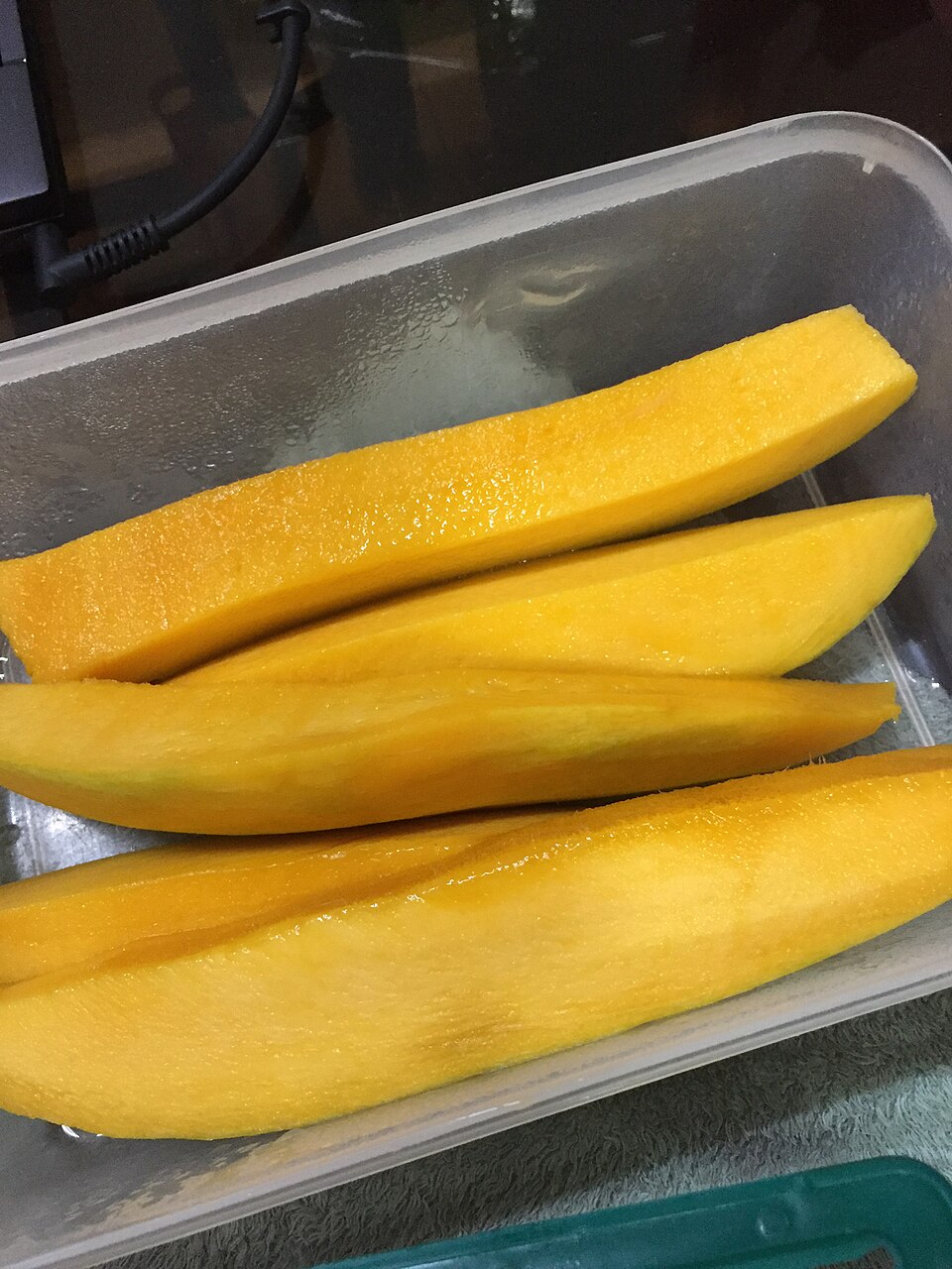 Several peeled mango slices arranged in a container.