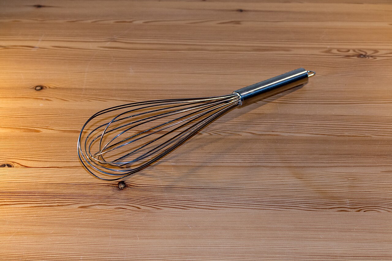 A wire balloon whisk resting on a wooden surface.