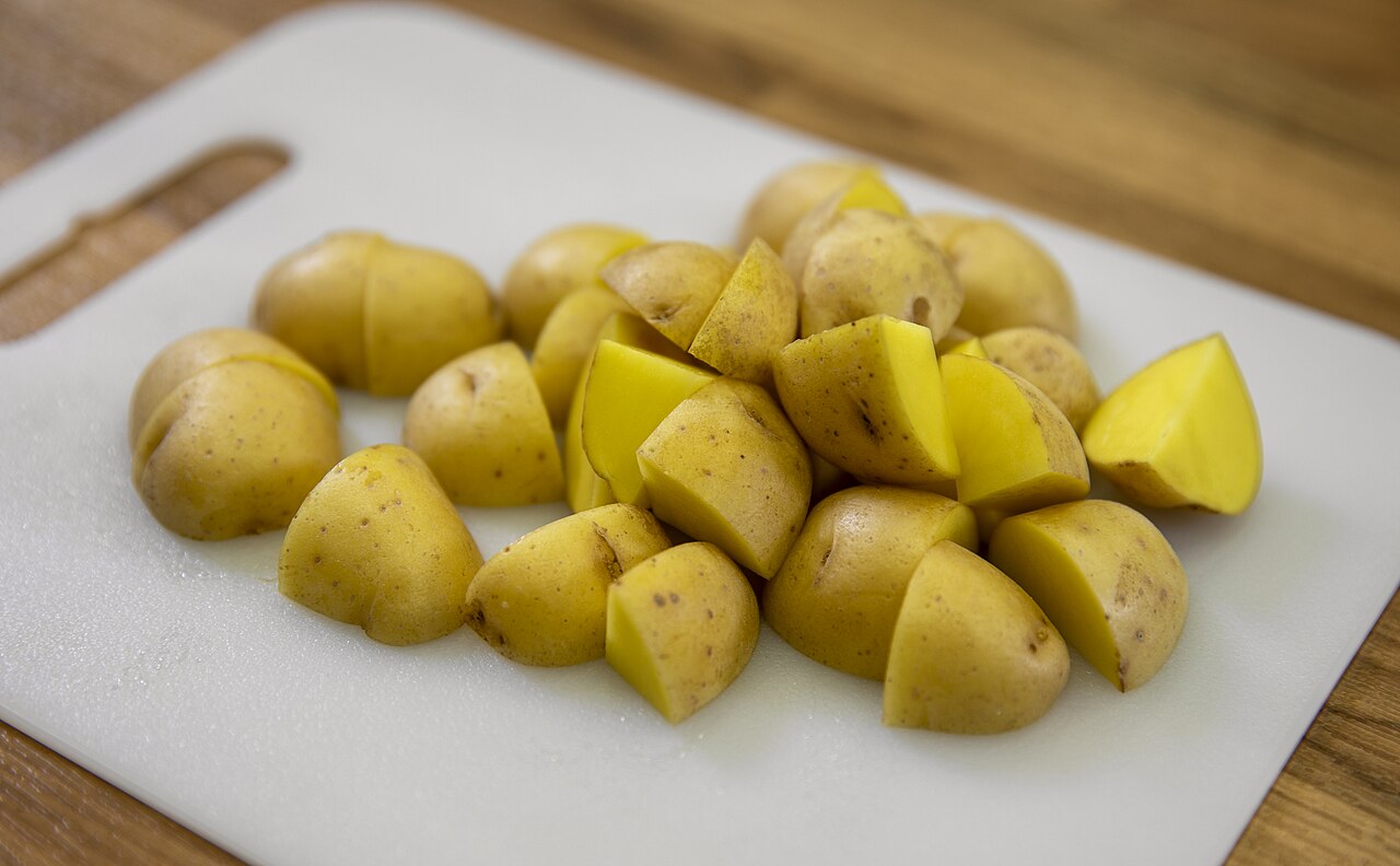 Cut yellow potatoes and halves on a white cutting board.